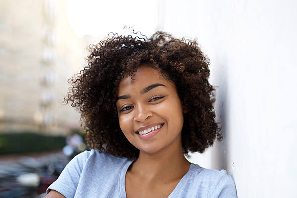 A smiling woman with curly hair, wearing a casual top, against a blurred background.