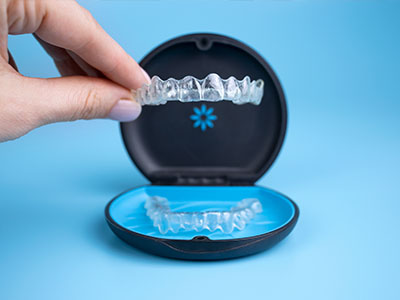 The image shows a person s hand holding an open case revealing a set of clear, plastic aligners.